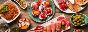 Cuatro platos con jamón, salchichón y otros embutidos y tres cuencos con aceitunas y otros alimentos