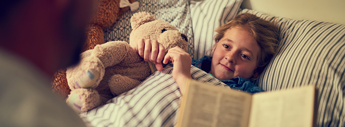 Niño acostado sonríe mientras le leen un cuento