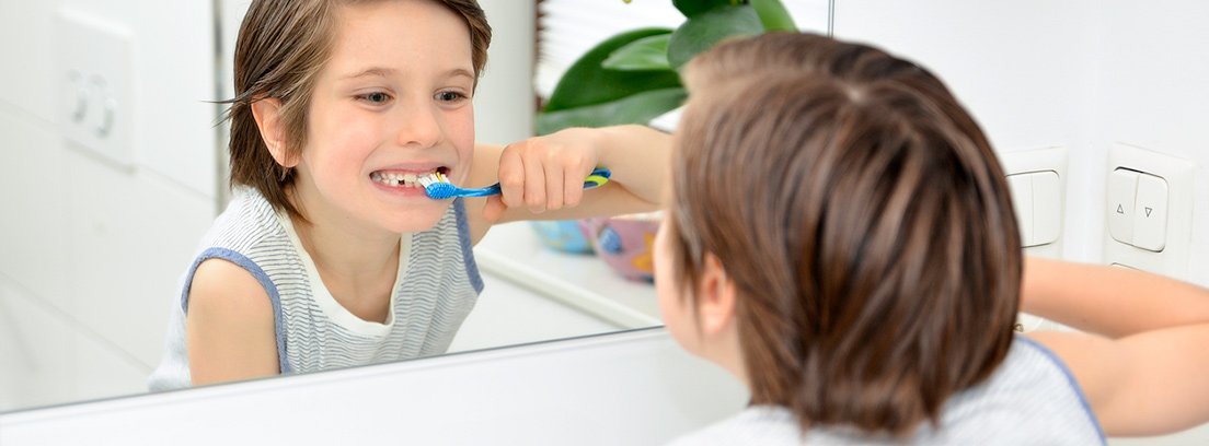 Un niño frente a un espejo lavándose los dientes