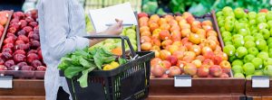 Mujer en el mercado con la lista de la compra y un cesto lleno de verduras