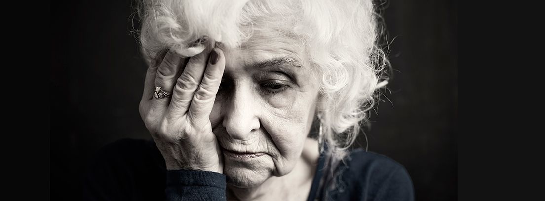 mujer mayor triste con la mano en la cara en fondo negro
