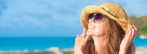 Mujer con gafas de sol sonríe cara al sol sujetando su sombrero