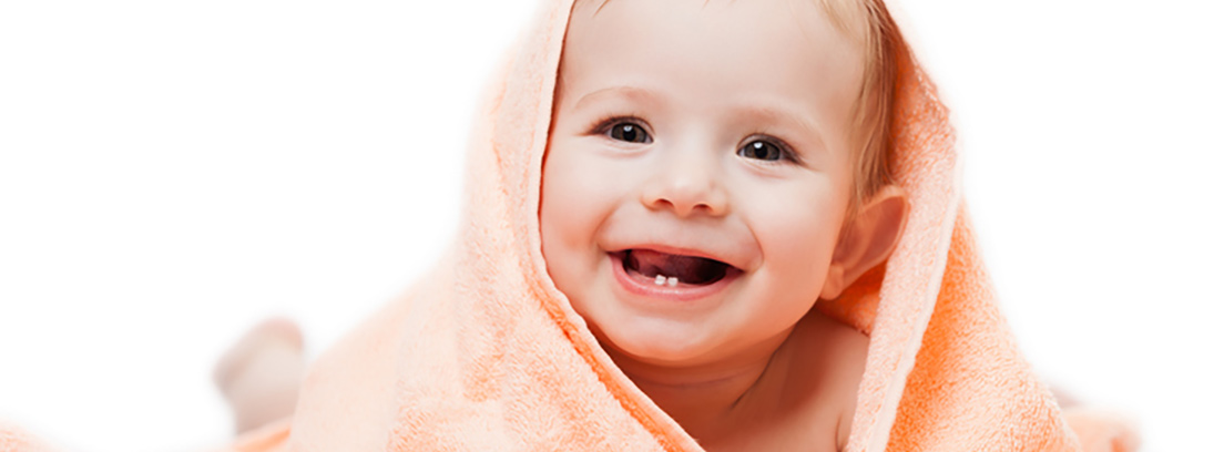 Bebé con una manta naranja sonriendo a la cámara con dos dientes solo