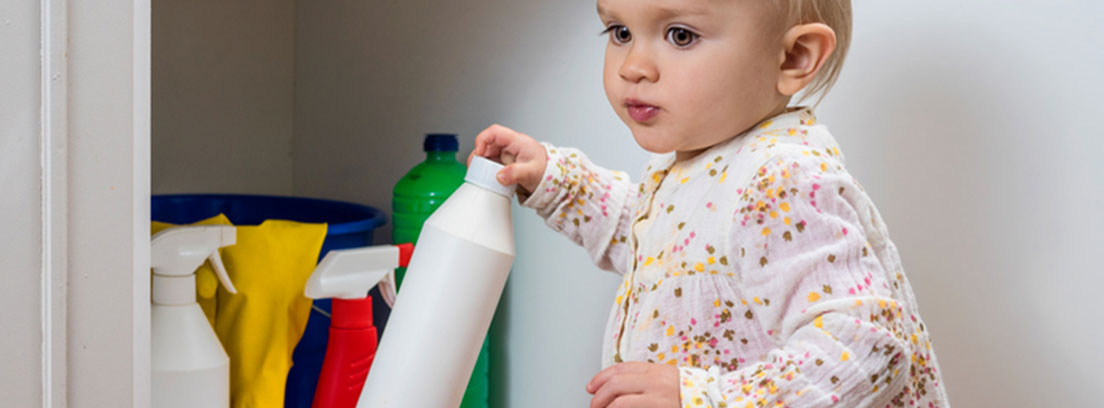 Bebé cogiendo una botella del armario de los productos de limpieza