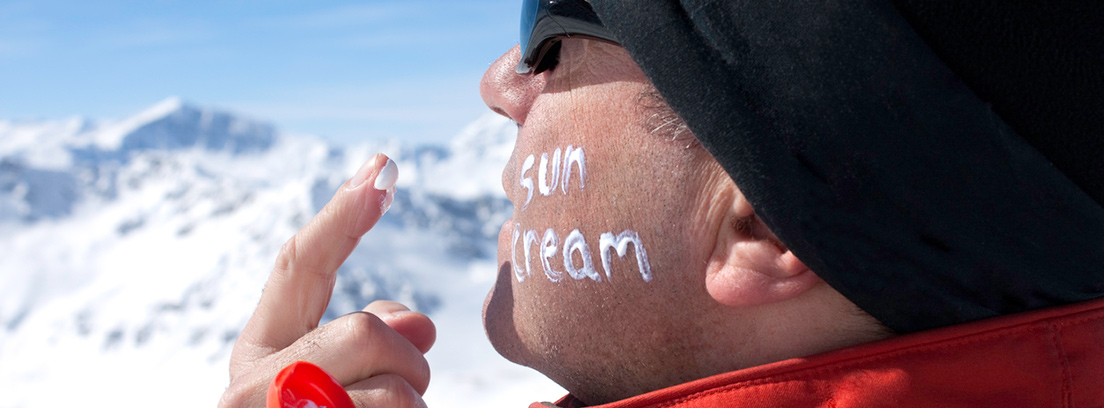Un esquiador se aplica crema solar en la cara escribiendo el texto "sun cream" con la ella