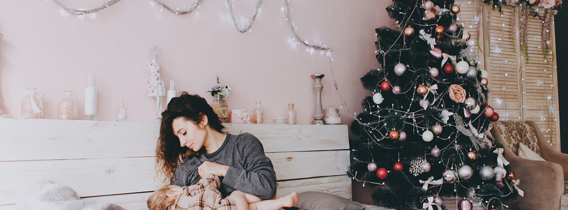 Una mujer da el pecho a su bebé en una habitación con decoración navideña