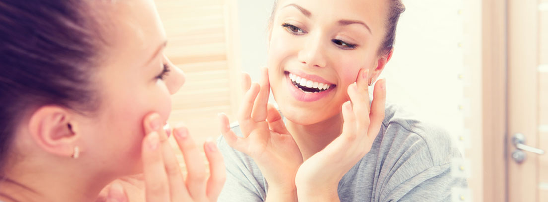 Mujer sonriente aplicándose una crema en la cara