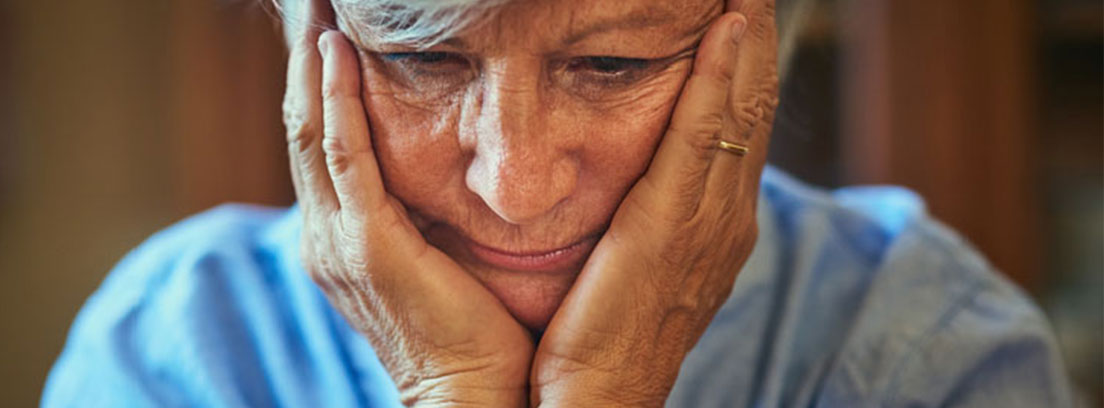 Mujer mayor con la mirada perdida, sujetando su cabeza con las manos