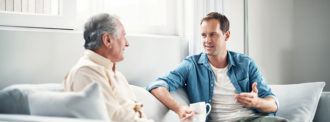 Un joven y un anciano charlan con una taza de café en un sofá