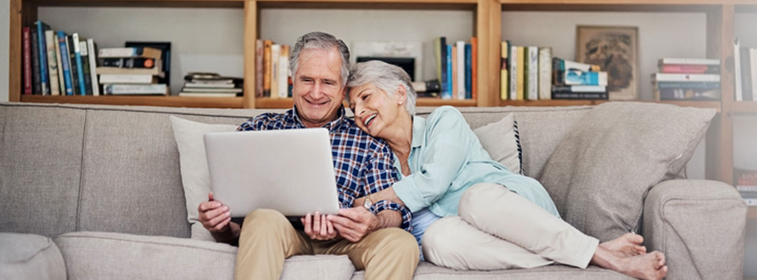 Una pareja feliz de séniors con un ordenador e Internet mayormente
