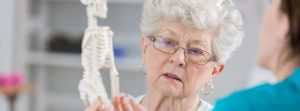 Una enfermera le enseña un esqueleto a una señora mayor