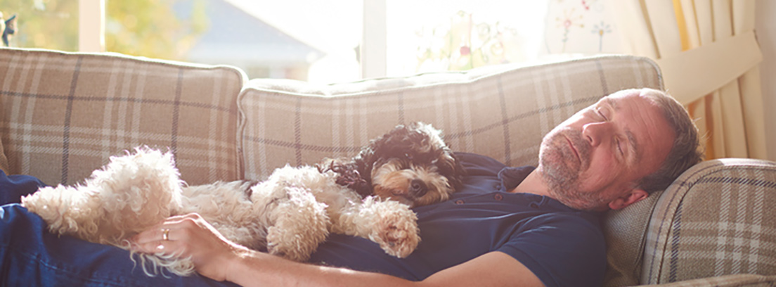 Un señor duerme la siesta en el sofá con su perro encima