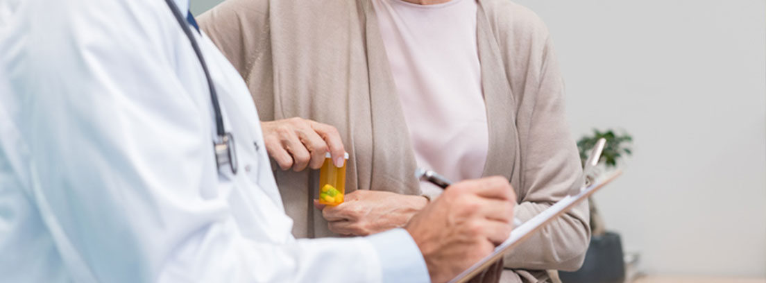 Mujer tomándose una pastilla mientras el medico escribe en una libreta