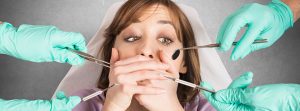 Mujer con miedo tapándose la boca mientras unas manos de dentista intentar atenderla