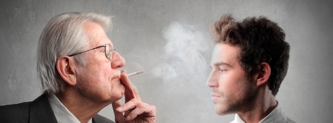 hombre mayor echando humo de tabaco a la cara de un joven