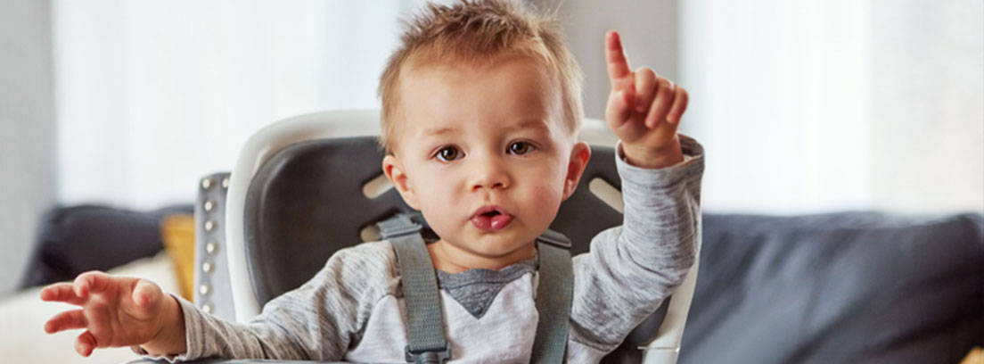 Bebé sentado en una trona señalando hacia arriba con su dedo índice