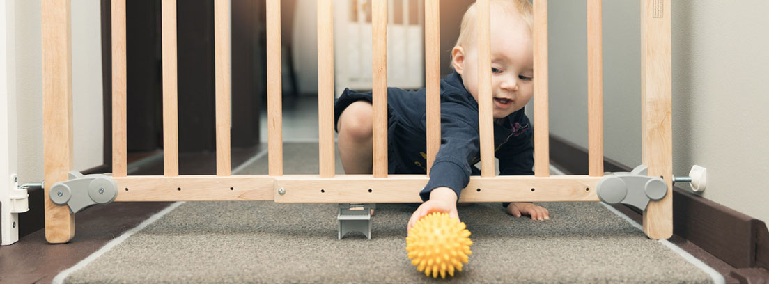 Casa segura para bebés: bebé cogiendo una pelota a través de una vaya de seguridad para escaleras