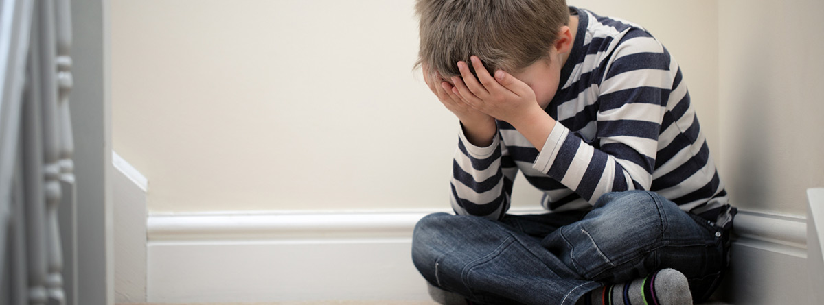 Ansiedad infantil: niño sentado en las escaleras con las manos tapándose la cara