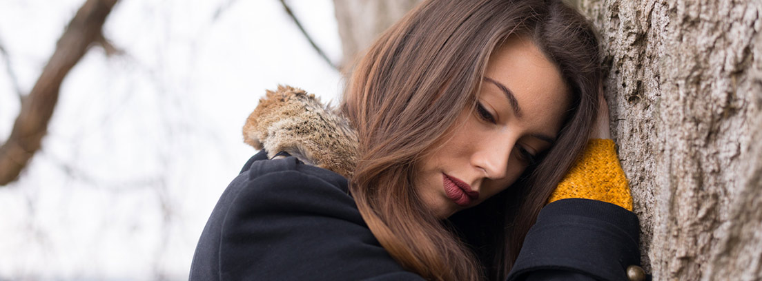 mujer deprimida apoyada en un árbol en otoño