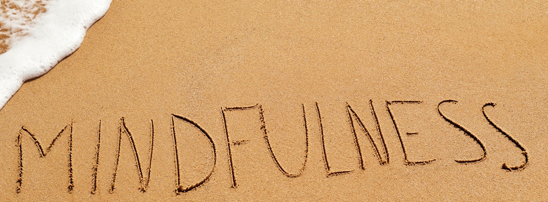 Mindfulness escrito en la arena de una playa