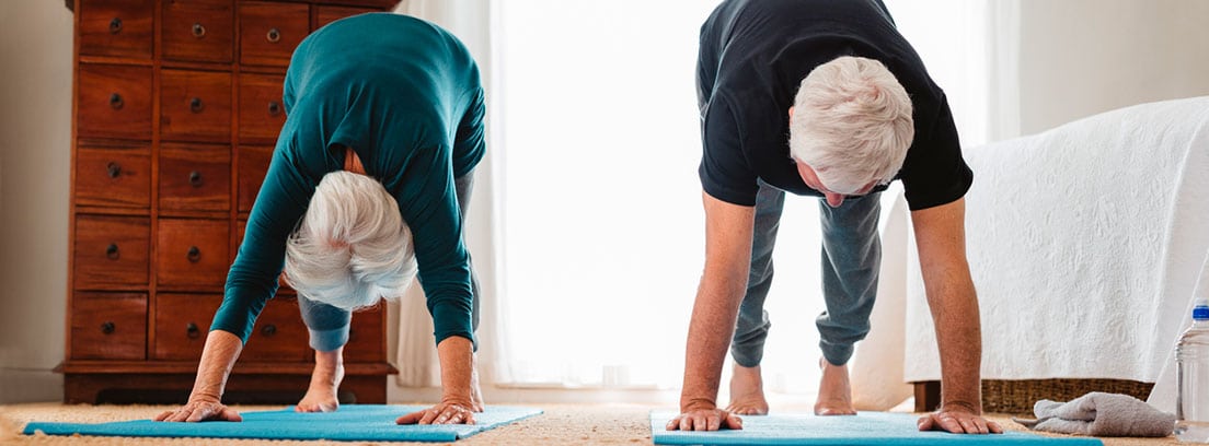 Ejercicio para seniors: pareja de personas mayores practicando ejercicio en el dormitorio