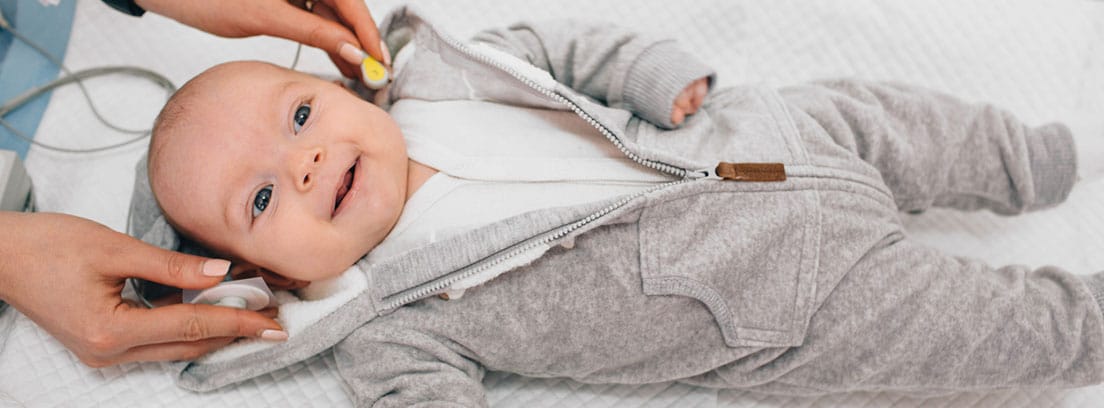 Otitis media en bebés: bebé tumnado en camilla y doctor mirándole el oído