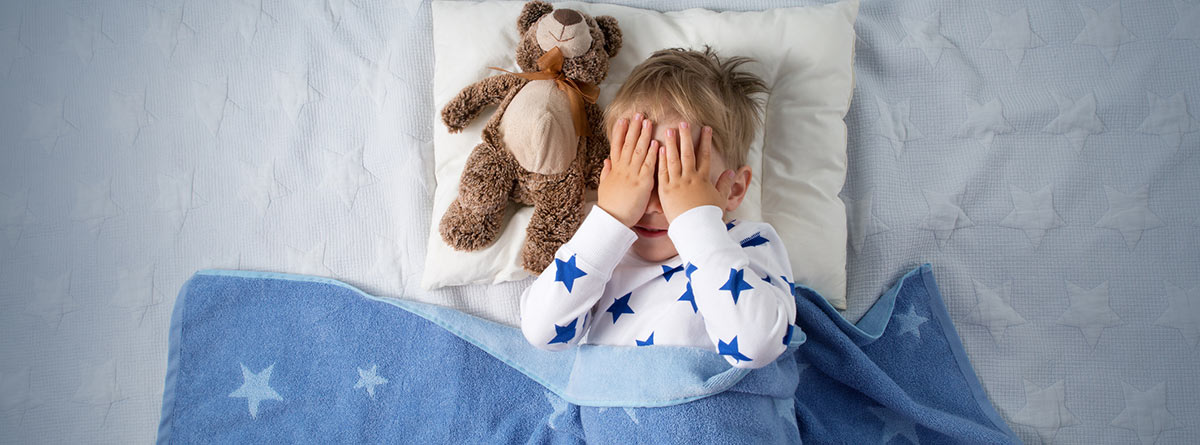 Pesadillas y terrores nocturnos: niño en la cama con las manos tapándose la cara y un osito de peluche a su lado