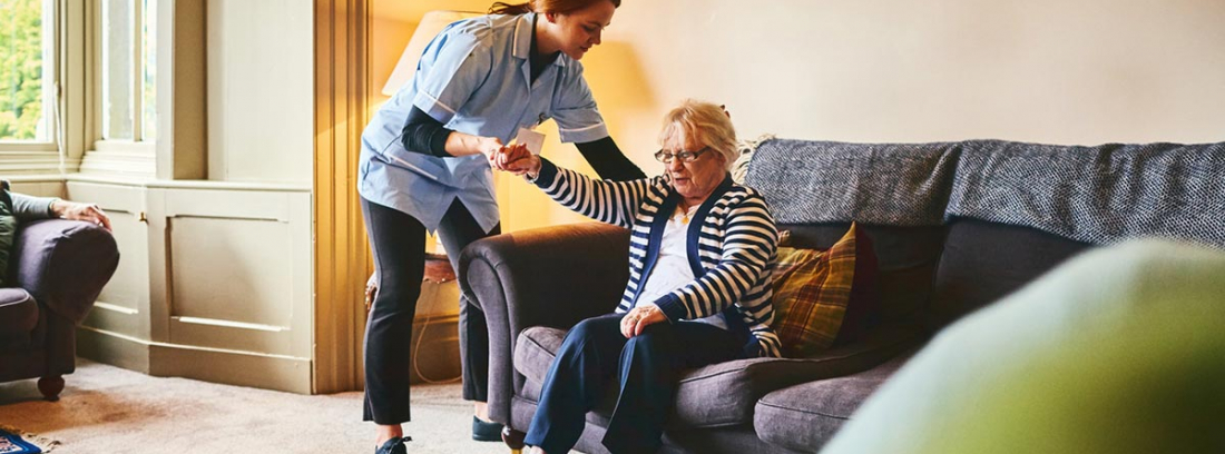 Síndrome de inmovilidad en personas mayores: cuidadora ayudando a levantarse del sofá a una mujer mayor