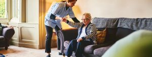 Síndrome de inmovilidad en personas mayores: cuidadora ayudando a levantarse del sofá a una mujer mayor
