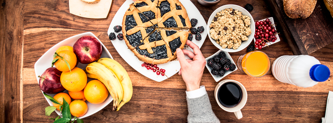 Mesa de madera con diferentes alimentos: tardas, frutos secos, fruta variada, etc.