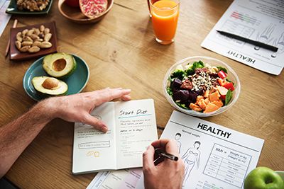 manos escribiendo una dieta encima de una mesa con diferentes alimentos