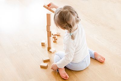niña sentada en el suelo de espaldas con las piernas en w jugando con tacos de madera