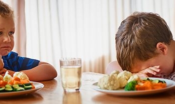 dos niños sentados en la mesa comiendo verduras