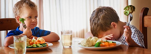dos niños sentados en la mesa comiendo verduras