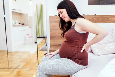 mujer embarazada sentada en la cama con dolor de lumbares