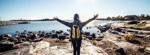 Mujer con mochila en la playa y con los brazos abiertos de espaldas