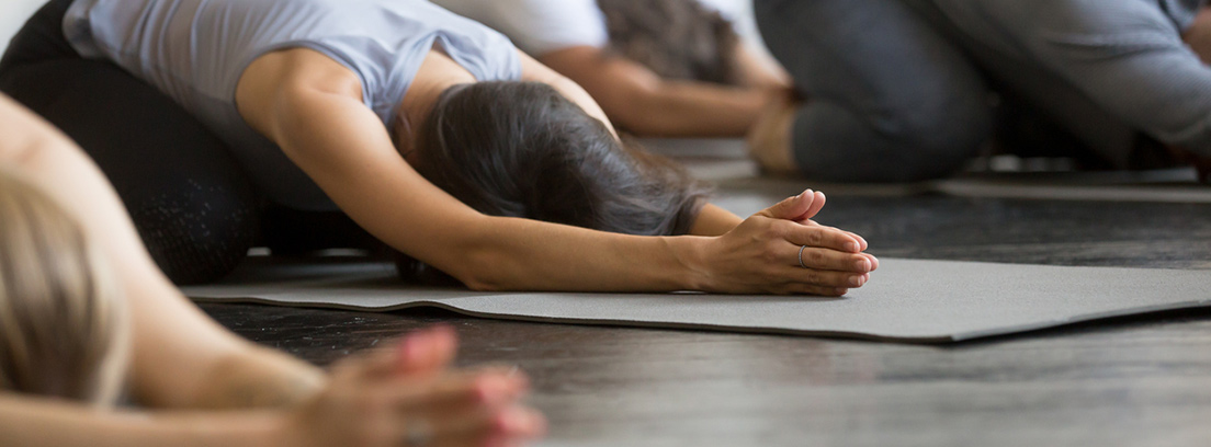 Grupo de personas haciendo una postura de yoga en el suelo con una esterilla