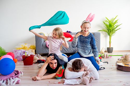 padres tumbados en el suelo con las hijas encima de ellos jugando en una habitación con juguetes