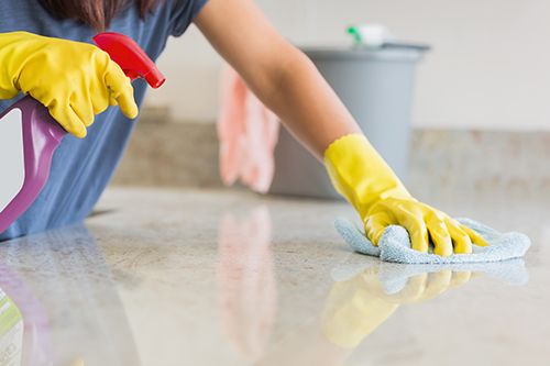 persona limpiando una encimera con guantes puestos y producto limpiador