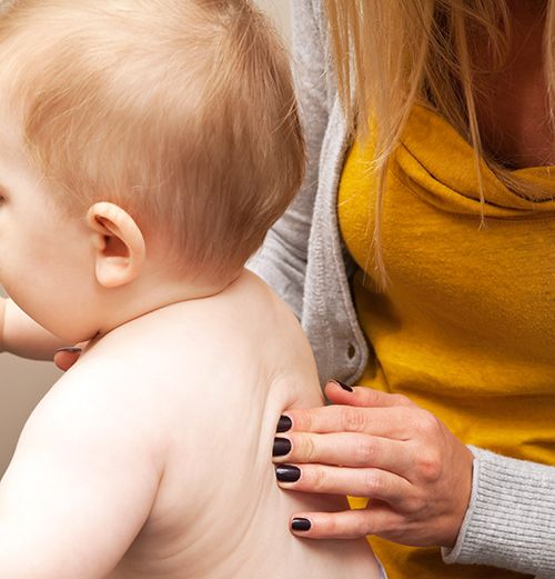 manos de mujer realizando un masaje en la espalda a un bebé