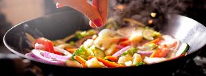 mano condimentando verduras en un wok