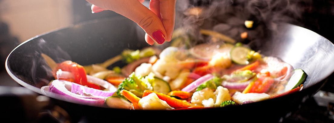 mano condimentando verduras en un wok