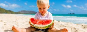 niños rubio en la playa con media sandia en las manos