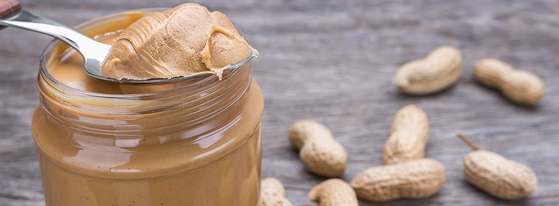 tarro de crema de cacahuete y cacahuestes alrededor