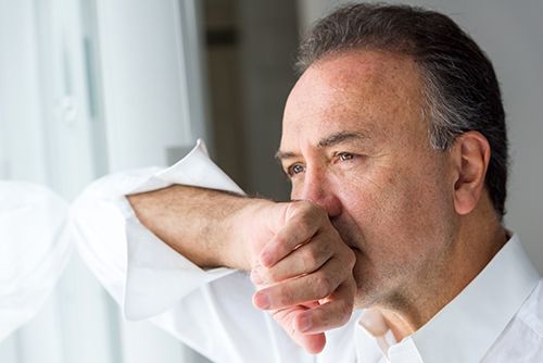 hombre mirando por la ventana con la mano en la boca, con expresión de culpa