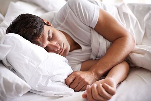 chico joven durmiendo de lado con sábanas blancas