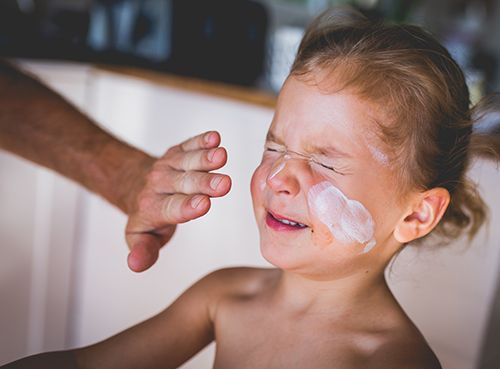 mano echando crema en la cara de una niña