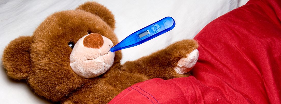 oso de peluche tumbado en la cama con un termómetro azul en la boca