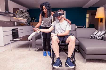 paciente en silla de ruedas con una raqueta y gafas de realidad virtual, con chica ayudándole