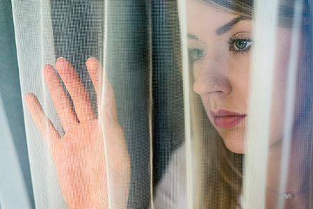 mujer con cara triste mirando a través de una cortina